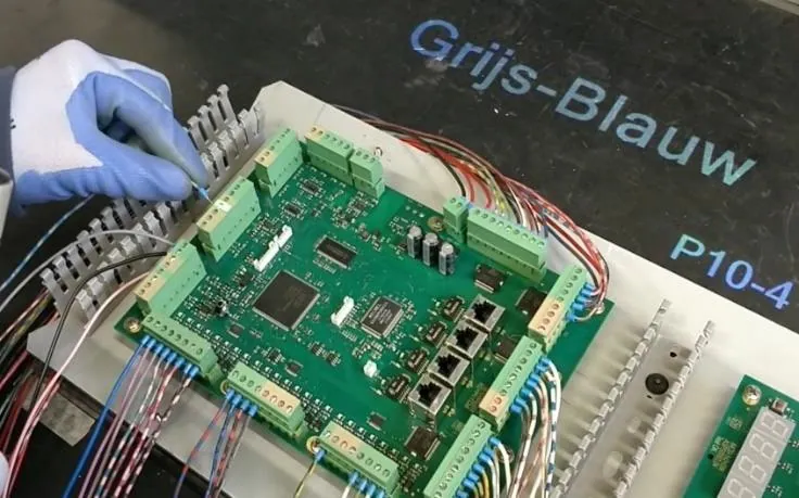 Operator connecting colored wires to the terminals of a circuit board, with a projected color code on the workbench