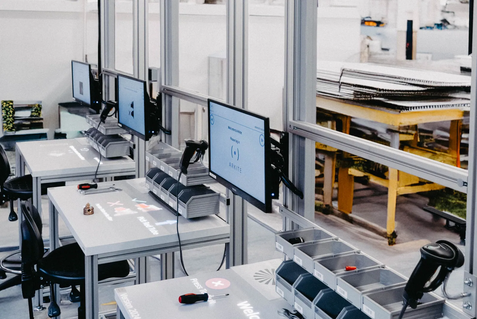 A row of Arkite workstations with projected instructions on the workbench, operator screens, picking bins and barcode scanners