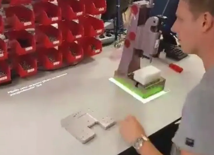 Operator at a workbench with a green projected outline marking where to place a part in a fixture, picking bins in the background