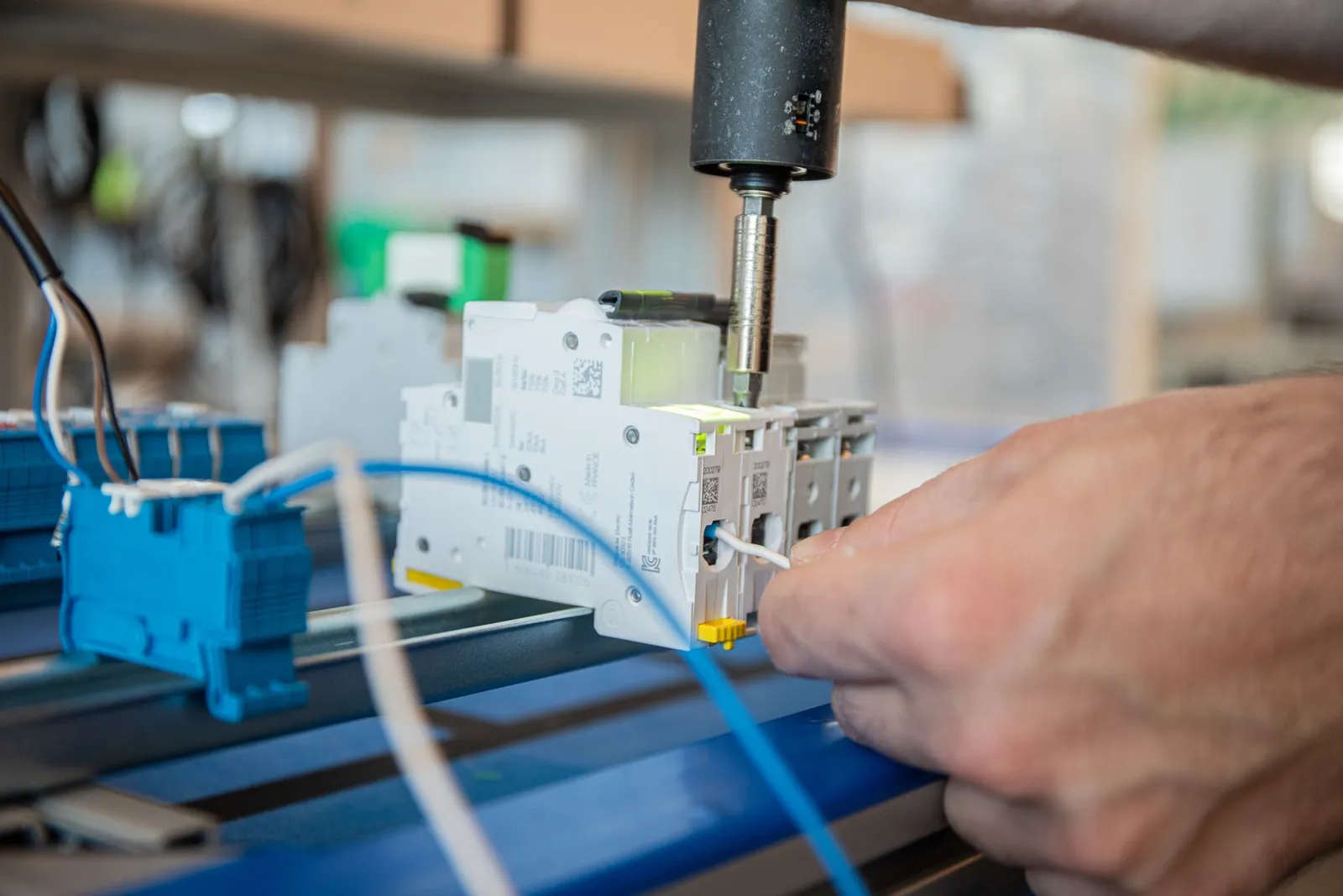 Smart screwdriver tightening a terminal on a circuit breaker while the operator positions a cable, with a projected highlight on the target