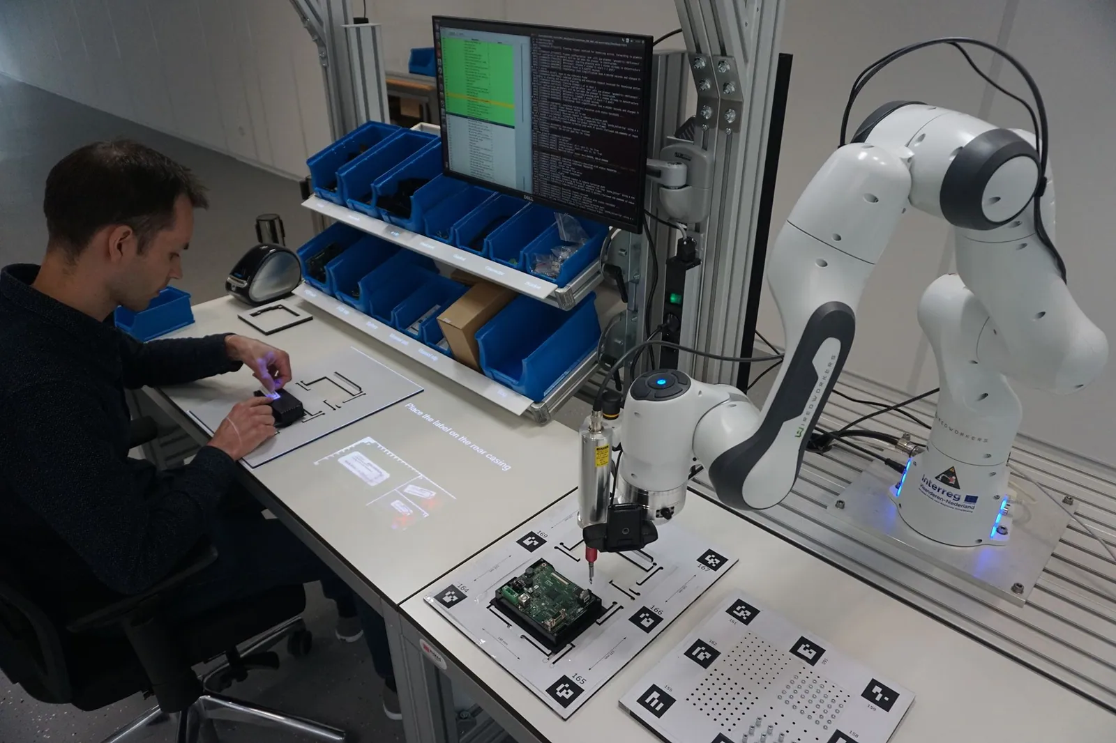 Operator working at an Arkite workstation with projected instructions next to a circuit board in a fixture
