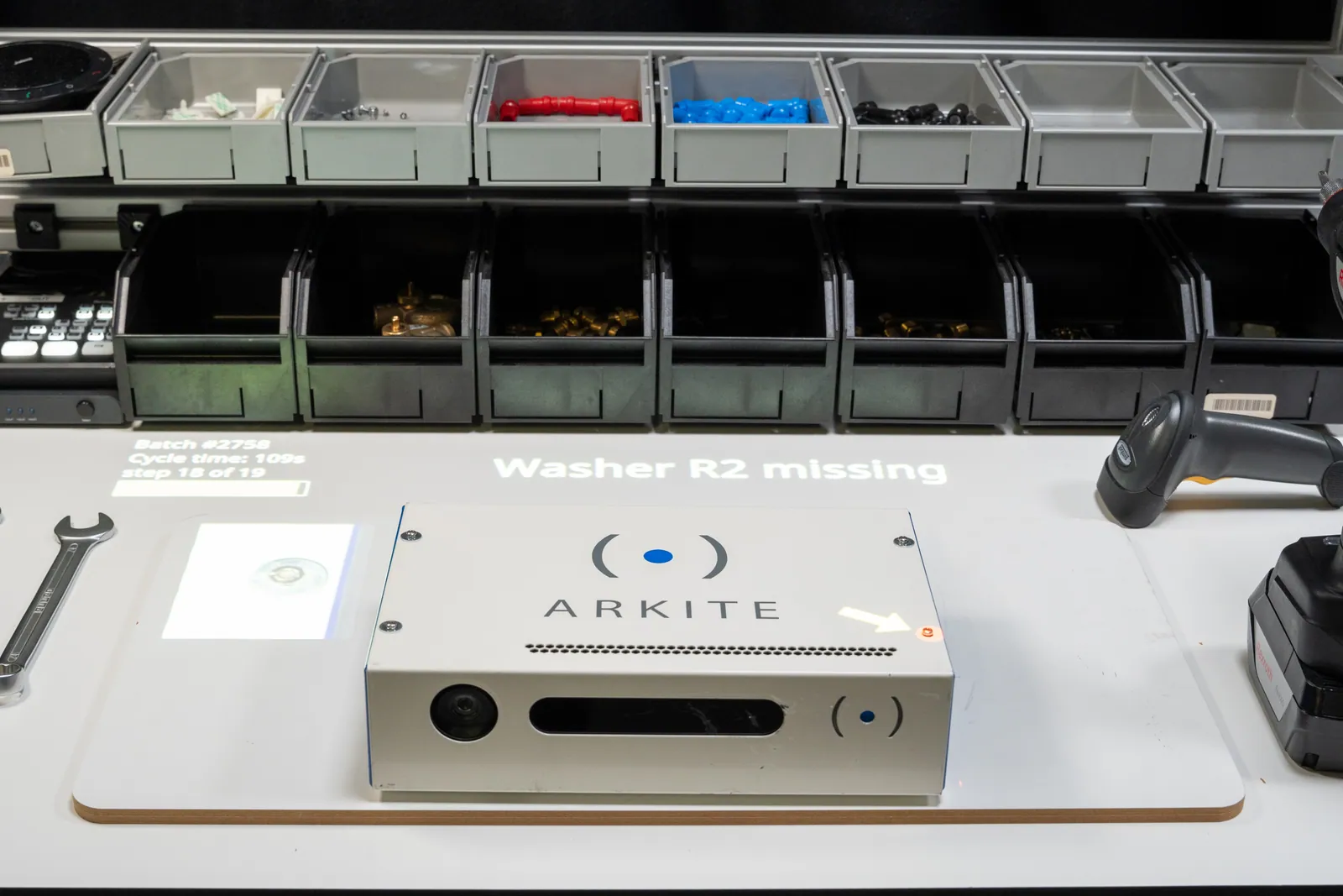 Arkite workstation projecting a message that a washer is missing during assembly, next to parts bins and a barcode scanner